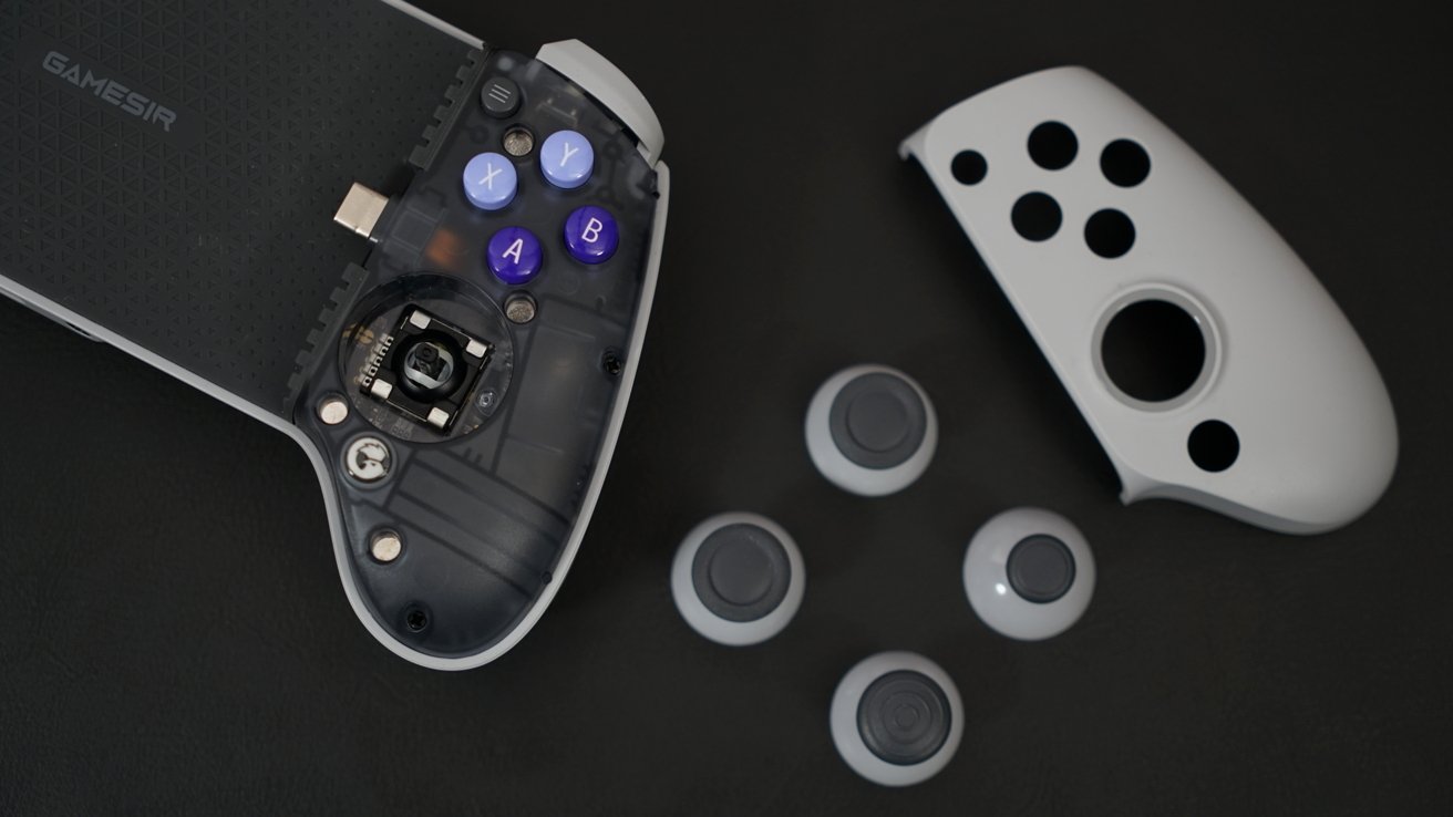 Контроллер GameSir со снятой лицевой панелью лежит рядом с серой лицевой панелью и четырьмя джойстиками. Прозрачный пластик на контроллере показывает внутреннюю схему.