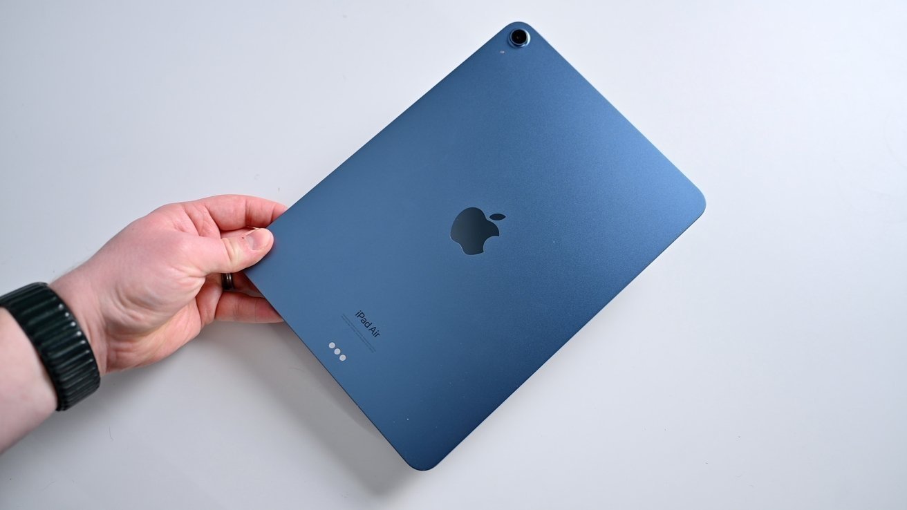 Рука держит синий планшет с логотипом Apple на оборотной стороне на светлом фоне.