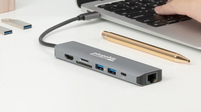 Концентратор USB-C, подключенный к ноутбуку с видимыми различными портами, расположен на столе рядом с ручкой.
