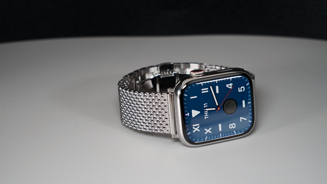 Apple Watch Series 9 из нержавеющей стали с синим циферблатом и крупными цифрами на браслете с миланскими звеньями на черном фоне.