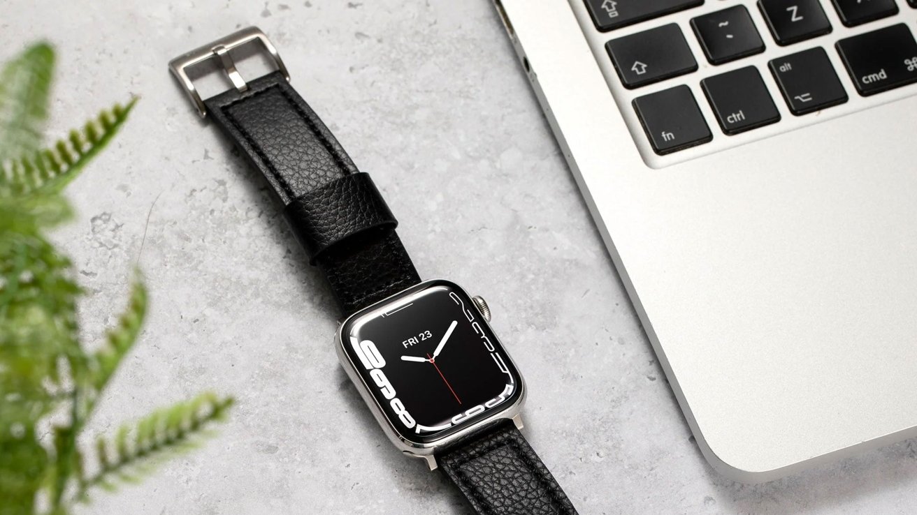 Apple Watch с кожаным ремешком Buck and Band рядом с клавиатурой MacBook на мраморной поверхности, с растением в мягком фокусе.