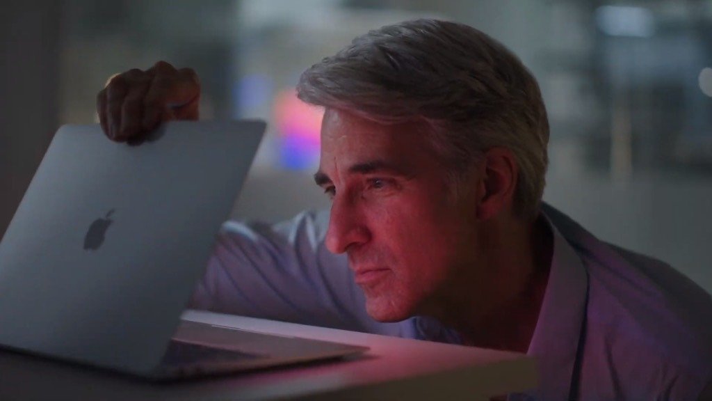 Зрелый мужчина с седыми волосами внимательно смотрит на светящийся экран ноутбука, слегка улыбаясь, в тускло освещенной комнате.