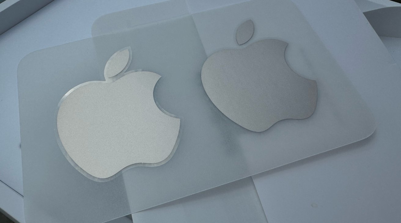 Две наклейки с логотипом Apple с серебряным градиентом, одна больше другой, на светлой поверхности.