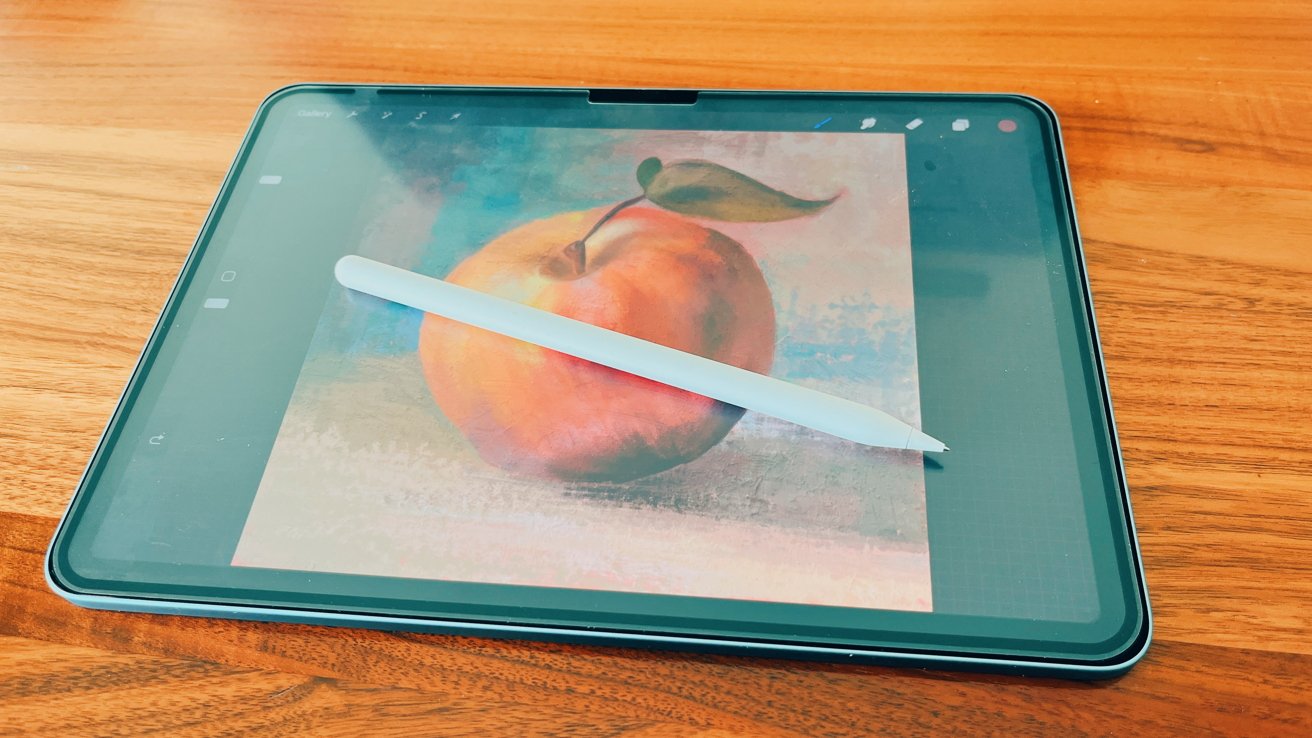 iPad, лежащий на деревянной поверхности, с изображением Apple со стилусом на экране.