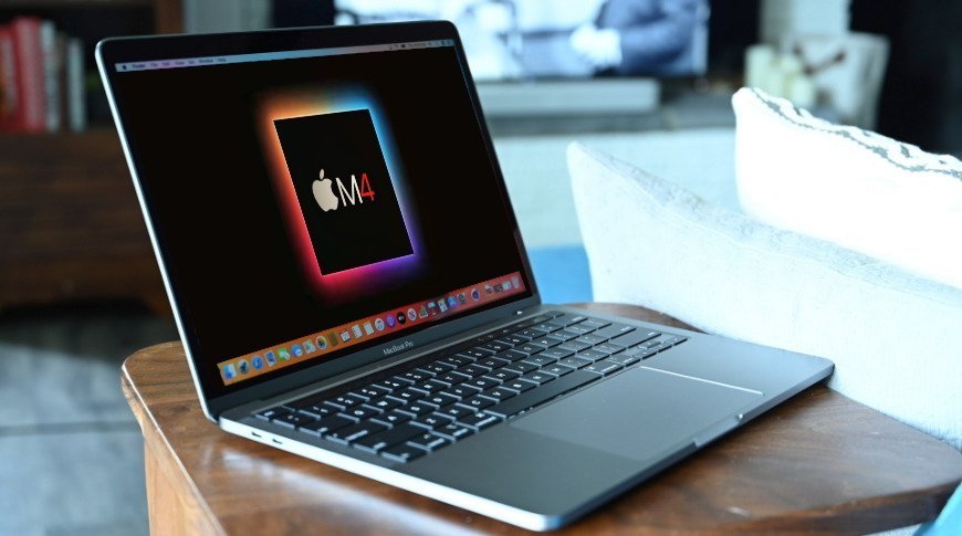 MacBook Pro на деревянном столе с цветным экраном с логотипом Apple M4 в уютной гостиной.