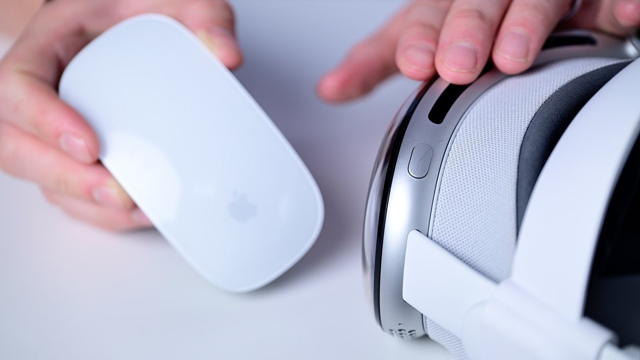 Руки держат белую компьютерную мышь и Apple Vision Pro на белой поверхности