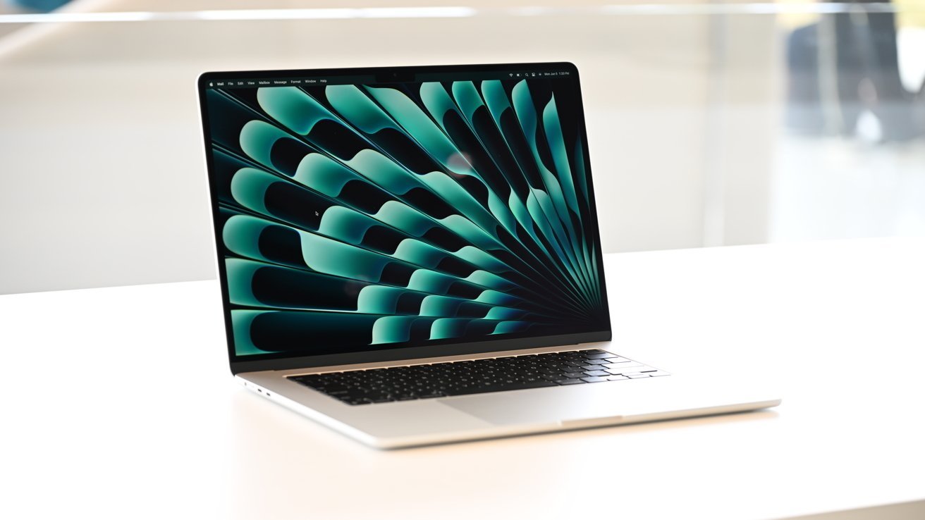 Ноутбук стоит на белой поверхности, на экране которого виден закрученный абстрактный зеленый узор.