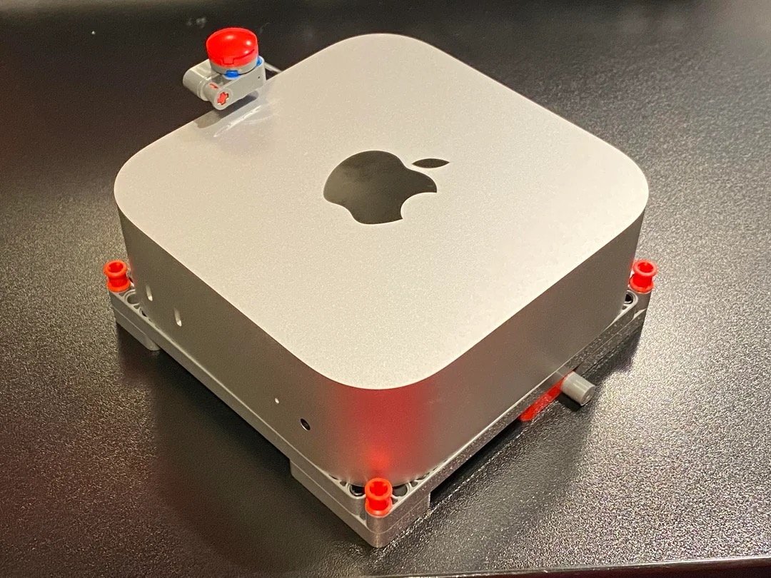 Модифицированный Apple Mac Mini с компонентами LEGO и маленькой красной кнопкой на темной поверхности.